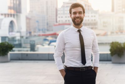 Man in a white shirt and necktie happily smiles against the background of the city